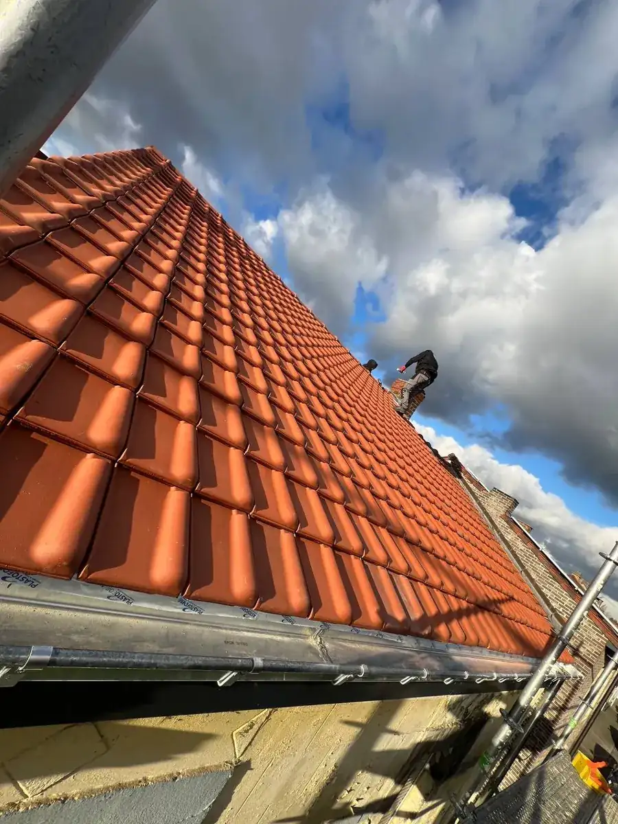 Dakdekker legt nieuwe rode kleipannen tijdens een dakrenovatie in Boortmeerbeek