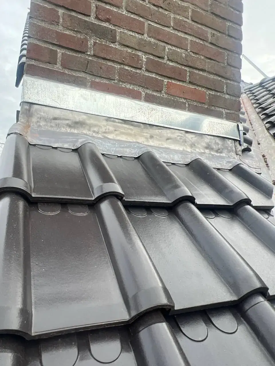 Nieuw loodwerk rond een schoorsteen op een vernieuwd pannendak in Kessel-Lo